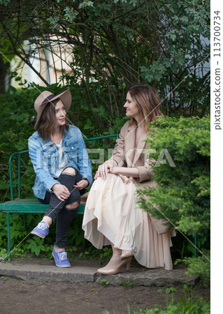 Nice friends talking and sitting on a park bench outdoors Nice friends talking and sitting on a park bench outdoors 113700734