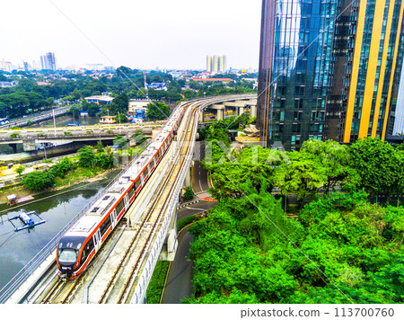 A red and white Jabodebek LRT train travels on a track. 113700760