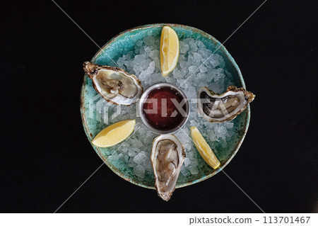 Oysters, served chilled with red wine cocktail sauce and fresh lemon on black wooden background Oysters, served chilled with red wine cocktail sauce and fresh lemon on black wooden background 113701467
