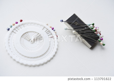 Multicolored pins on a white background. Pins and a sewing magnet. Multicolored pins on a white background. Pins and a sewing magnet. 113701822