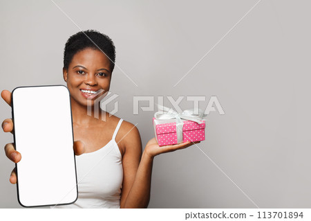 Nice female model with gift and smartphone with white empty blank screen display on gray studio 113701894