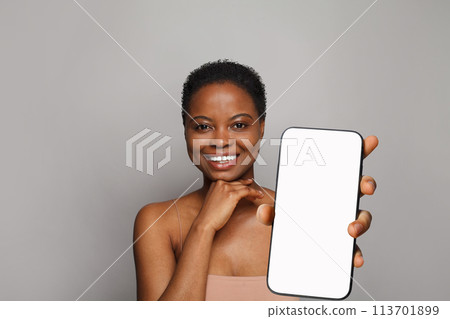 Cheerful healthy woman holding smartphone with white empty blank screen display on gray Cheerful healthy woman holding smartphone with white empty blank screen display on gray 113701899