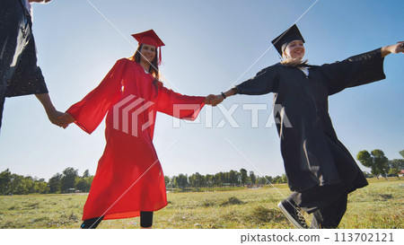 College graduates holding hands run in a round dance. College graduates holding hands run in a round dance. 113702121
