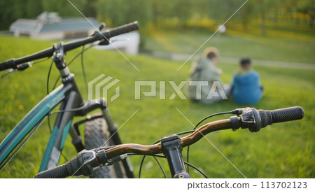 Two boys relaxing in the park in front of their bicycles. Two boys relaxing in the park in front of their bicycles. 113702123