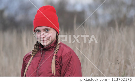 A teenage girl in red clothes touching dry grass in late fall. A teenage girl in red clothes touching dry grass in late fall. 113702176