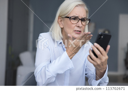 Mad businesswoman gawp at smart phone screen seated at workplace 113702671