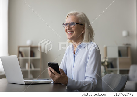 Overjoyed mature businesswoman laugh on message received at workplace Overjoyed mature businesswoman laugh on message received at workplace 113702772