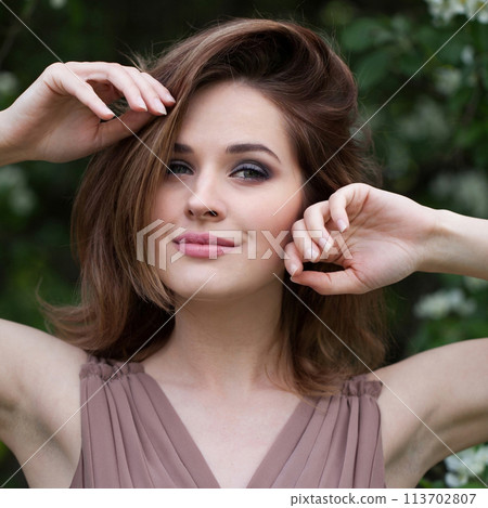 Elegant brunette lady outdoor portrait. Healthy woman against green blossom background 113702807