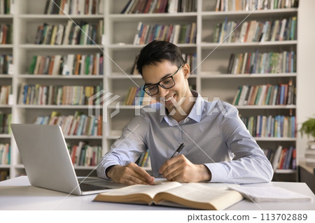 Smiling intelligent Indian student guy makes exercise in copybook Smiling intelligent Indian student guy makes exercise in copybook 113702889