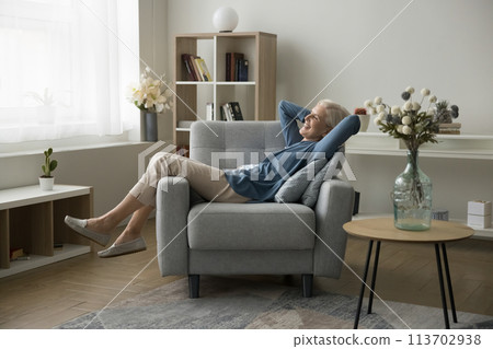 Peaceful happy older woman enjoys lazy weekend relaxing on armchair Peaceful happy older woman enjoys lazy weekend relaxing on armchair 113702938