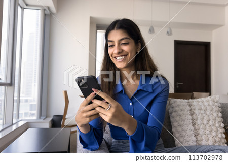 Positive excited young Indian woman typing on mobile phone 113702978
