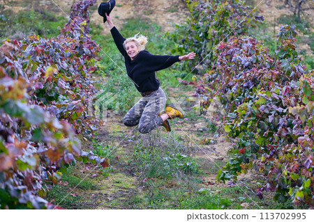 Joyful mature young blondy farmer woman jumping in a vineyard farmland. Joyful mature young blondy farmer woman jumping in a vineyard farmland. 113702995