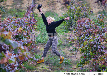 Joyful mature young blondy farmer woman jumping in a vineyard farmland. Joyful mature young blondy farmer woman jumping in a vineyard farmland. 113703006