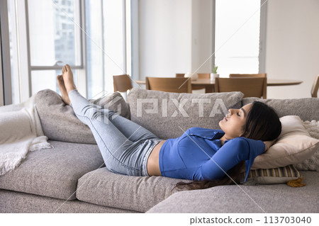 Calm relaxed young Indian woman resting on soft comfortable couch 113703040