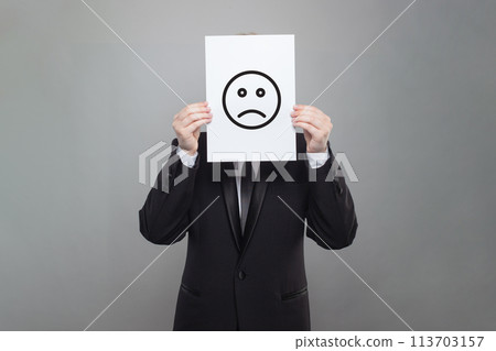 Sad emoticon on business person head on gray studio wall background Sad emoticon on business person head on gray studio wall background 113703157