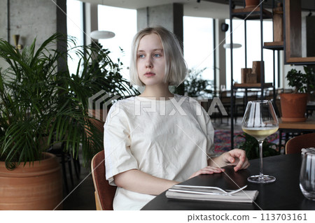 Romantic young woman sitting at table holding in hand glass of drink at restaurant.  113703161