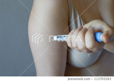 Woman making self injection with blue injection pen closeup. Medicine and treatment concept Woman making self injection with blue injection pen closeup. Medicine and treatment concept 113703263