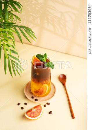 Americano coffee with orange juice (bumble) in a tall glass with ice and mint on a yellow background Americano coffee with orange juice (bumble) in a tall glass with ice and mint on a yellow background 113703684