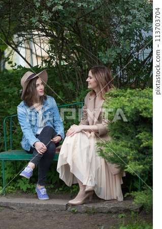 Pretty friends talking and sitting on a park bench outdoors 113703704