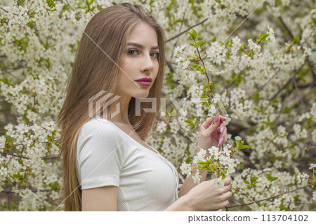 Nice fashion model with long brown hair and natural makeup against floral background outdoor 113704102