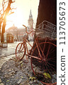 Old abandoned rust bicycle stands in the center of a European city with a view of the town hall and the square. Backlight from the sun. Late autumn or winter. Decline and decay. Vertical image. 113705673