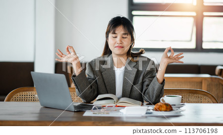 Professional woman meditates at her work desk to find calm amidst a busy schedule. Professional woman meditates at her work desk to find calm amidst a busy schedule. 113706198