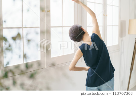 A woman in her 30s stretching by the window 113707303