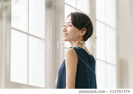 A woman in her 40s standing by the window 113707374