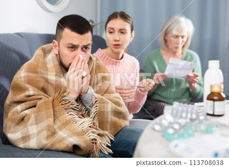 Sick man sitting on couch while his family trying to help Sick man sitting on couch while his family trying to help 113708038