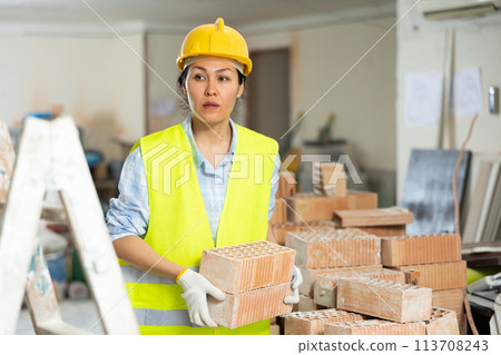 Female builder carrying bricks at renovating object 113708243