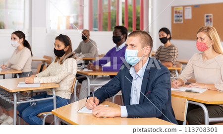 Group of students in protective mask listening attentively to teacher explaining material in the classroom Group of students in protective mask listening attentively to teacher explaining material in the classroom 113708301