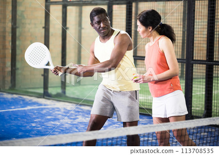 African american trainer teaches woman to play padel on tennis court 113708535