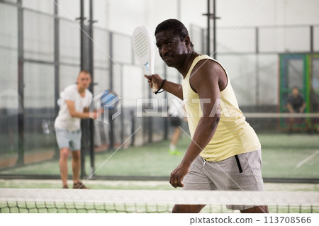 Sporty african american playing padel on indoor court 113708566