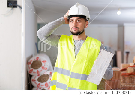 Frustrated worker in yellow vest and hard hat is dissatisfied with the way walls are plastered 113708713