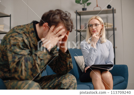 Soldier and psychiatrist sitting on couch during therapy session. Man wearing military uniform. Male warrior with ptds talking to psychiatrist. Soldier and psychiatrist sitting on couch during therapy session. Man wearing military uniform. Male warrior with ptds talking to psychiatrist. 113709240