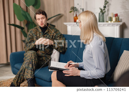 Soldier and psychiatrist sitting on couch during therapy session. Man wearing military uniform. Male warrior with ptds talking to psychiatrist. 113709241