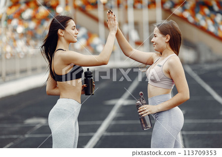 Beautiful girls at the stadium. Sports girls in a sportswear. People with bottle of water. Beautiful girls at the stadium. Sports girls in a sportswear. People with bottle of water. 113709353