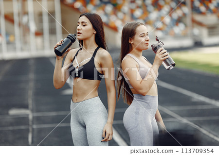 Beautiful girls at the stadium. Sports girls in a sportswear. People with bottle of water. Beautiful girls at the stadium. Sports girls in a sportswear. People with bottle of water. 113709354