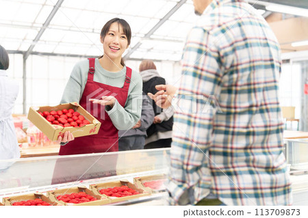 一位穿著圍裙的年輕女店員微笑著賣草莓 113709873