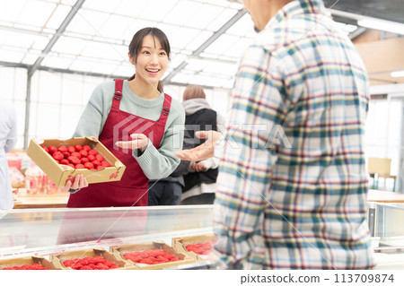 一位穿著圍裙的年輕女店員微笑著賣草莓 113709874
