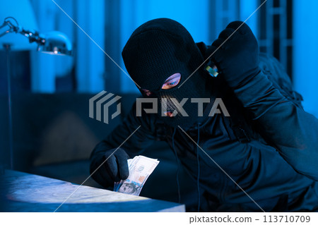 Thief counting money dollars during a burglary Thief counting money dollars during a burglary 113710709