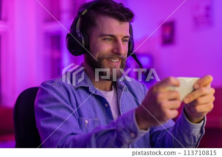 Man playing games on smartphone with headset Man playing games on smartphone with headset 113710815