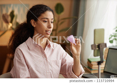 Portrait of multiracial young woman holding menstrual cup and recording videos via smartphone 113710994