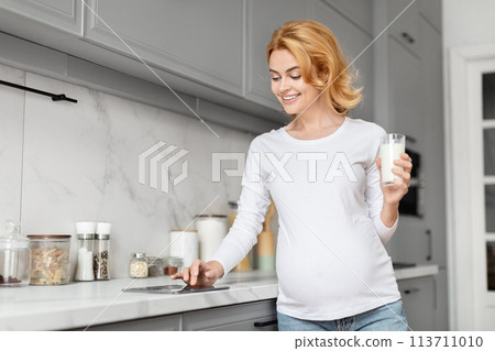 Pregnant woman holding a glass of milk in kitchen 113711010