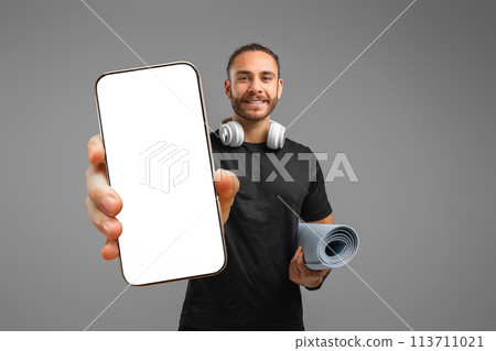 Happy man showing smartphone screen on grey background Happy man showing smartphone screen on grey background 113711021