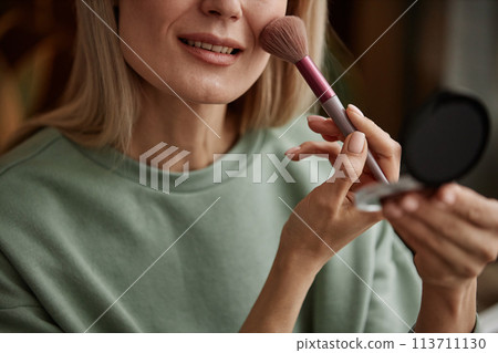 Close up of smiling woman doing make up looking in compact mirror and applying blush copy space Close up of smiling woman doing make up looking in compact mirror and applying blush copy space 113711130