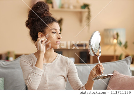 Side view portrait of young Middle eastern woman applying moisturizing face mask and looking in mirror at home Side view portrait of young Middle eastern woman applying moisturizing face mask and looking in mirror at home 113711159
