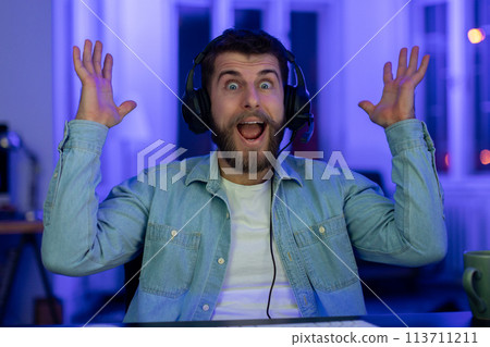 Excited gamer throws hands in surprise at home 113711211