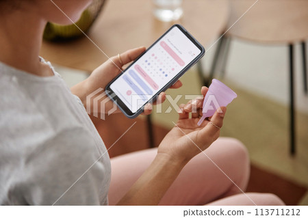 Closeup of unrecognizable girl holding menstrual cup and smartphone with period tracker app on screen copy space Closeup of unrecognizable girl holding menstrual cup and smartphone with period tracker app on screen copy space 113711212