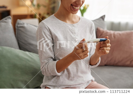 Minimal cropped shot of smiling young woman holding pregnancy test sitting on sofa at home copy space Minimal cropped shot of smiling young woman holding pregnancy test sitting on sofa at home copy space 113711224